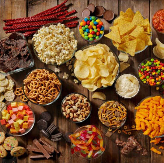 Grickalice-razne-kokice-čips-integralne-grisine-smoki-slani-štapići-kikiriki-snack mix-zdrave-slane-pločice-u-raznim-činijama-na-drvenom-stolu.